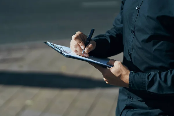 Un hombre con documentos en sus manos en sus camisas negras en la calle con un bolígrafo en la mano — Foto de Stock