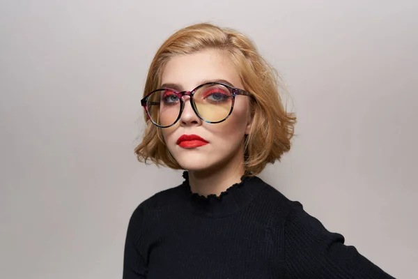 Blonde with short hairstyle with glasses red lips black jacket light background cropped view
