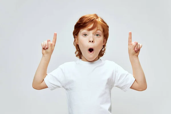 Kind mit roten Haaren zeigt Zeigefinger nach oben und weißes T-Shirt — Stockfoto