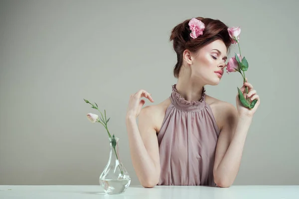 Femme romantique avec des fleurs dans ses cheveux et vase avec une fleur rose table de fond clair Images De Stock Libres De Droits