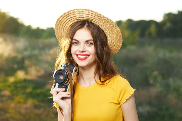 Senyum wanita dengan kamera di tangan mengenakan topi bibir merah warna kuning t-shirt alam — Stok Foto