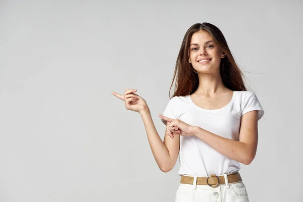 Uma mulher em uma camiseta branca mostra os dedos para o lado sorrir cabelos longos Espaço Copiar — Fotografia de Stock