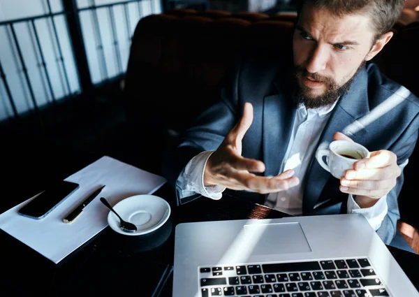 Uomo d'affari seduto in un caffè con una tazza di caffè tra le mani di fronte a una comunicazione tecnologia portatile — Foto Stock