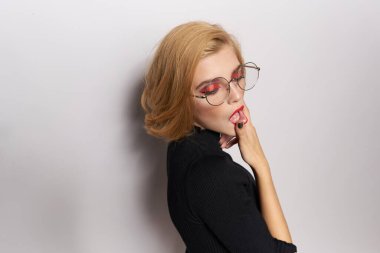 Gözlüklü sevimli sarışın, makyajlı, siyah ceketli açık renk arka plan duyguları olan.