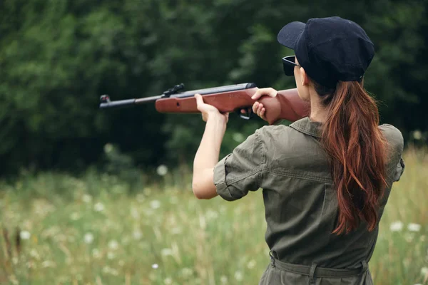 Kadın asker elinde silah tutuyor. Dikiz aynasından nişan alıyor. Yeşil ağaçlar. — Stok fotoğraf