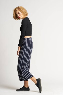 Siyah kazaklı, çizgili pantolonlu, güzel bir kadın. Moda kıyafetleri arka planda.