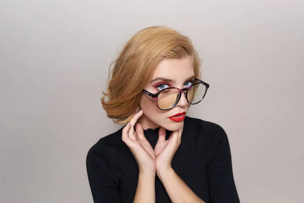 Blonde avec coiffure courte avec des lunettes lèvres rouges veste noire fond clair vue recadrée — Photo