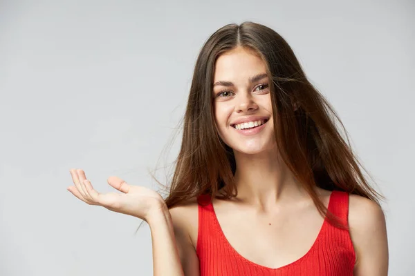 Boldog nő piros pólóban mutatja a kezét oldalra egy könnyű háttér — Stock Fotó