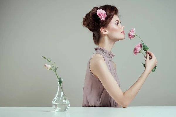 Femme romantique avec des fleurs dans ses cheveux et vase avec une fleur rose table de fond clair — Photo