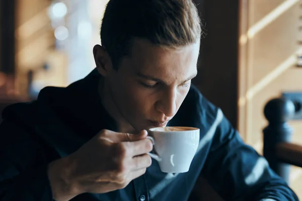 Businessman with a cup of coffee in a cafe and a dark shirt handsome face