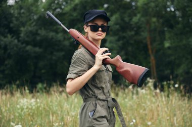 Kadın asker. Silah güneş gözlüklü yeşil bir tulum giyiyor. 