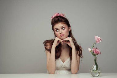 Beyaz elbiseli kadın sofrada oturuyor. Çiçekler, zarif tarz, hafif arka plan.