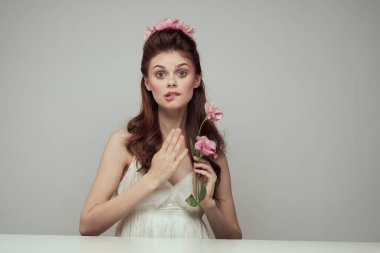 Beyaz elbiseli kadın sofrada oturuyor. Çiçekler, zarif tarz, hafif arka plan.