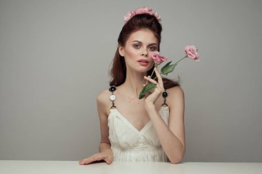 Beyaz elbiseli kadın sofrada oturuyor. Çiçekler, zarif tarz, hafif arka plan.