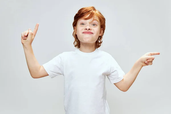Rothaariger Junge mit einem dummen Gesichtsausdruck gestikuliert mit den Händen, um mit dem Finger in Richtung Copy Space zu zeigen. — Stockfoto