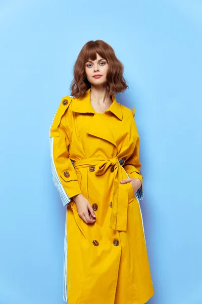Senhora em um casaco amarelo com botões em um fundo azul segura a mão no bolso — Fotografia de Stock
