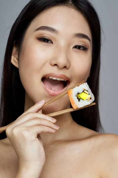 Γυναίκα με ξυλάκια κοντά στο στόμα, σούσι κυλά γυμνοί ώμοι. — Φωτογραφία Αρχείου