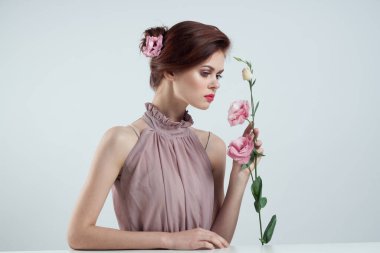 Saçında çiçekler, vazosunda pembe çiçekli arka plan masası olan romantik bir kadın.