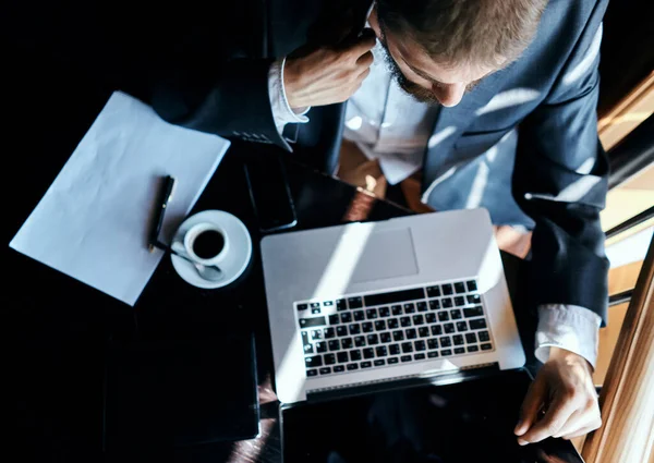 Uomo d'affari seduto in un caffè di fronte a un computer portatile documenti tazza di caffè esecutivo vista dall'alto tecnologia stile di vita — Foto Stock