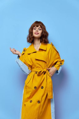 Sarı ceketli kadın ellerini mavi izole bir arka planda gezdiriyor. 