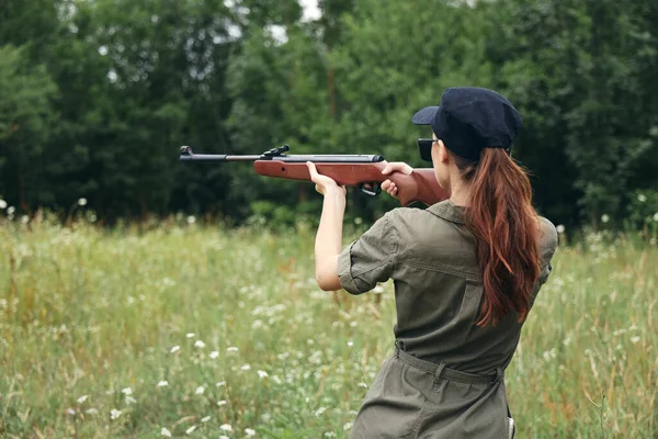 Mulher arma com o objetivo de caça visão traseira em macacões verdes ao ar livre — Fotografia de Stock