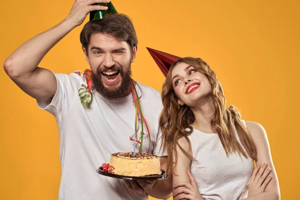 Uomo e donna compleanno torta festiva sfondo giallo e tappi sul headv — Foto Stock