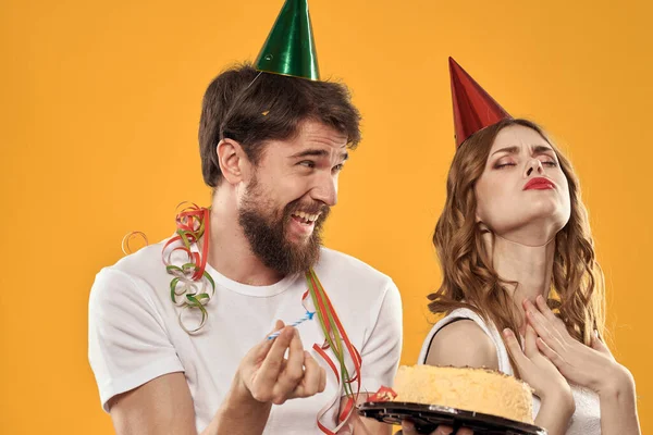 Homme et femme anniversaire gâteau festif fond jaune et casquettes sur la tête — Photo
