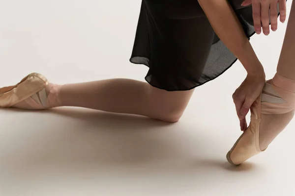 バレリーナは彼女の足の上にポイントシューズを置きますホワイトリボンモデルダンス光の背景. — ストック写真