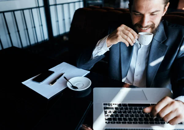 Uomo d'affari seduto in un caffè con una tazza di caffè tra le mani di fronte a una comunicazione tecnologia portatile — Foto Stock