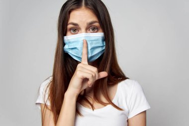 Yüzüne tıbbi maske takan bir kadın parmağıyla kafasına yakın duruyor. 