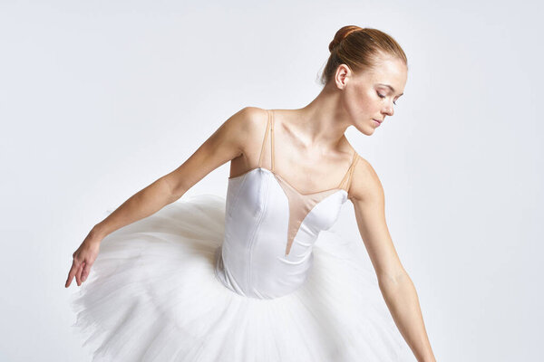 Ballerina in a white tutu dance performed on a light background. High quality photo