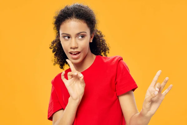 Menina bonito em uma camiseta vermelha em um fundo amarelo gestos com as mãos — Fotografia de Stock