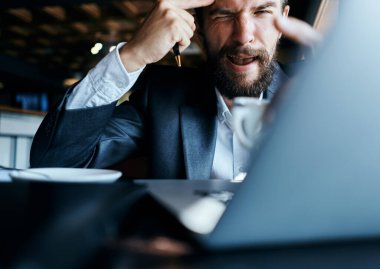 Bir kafede elinde bir fincan kahveyle oturan bir iş adamı dizüstü bilgisayar teknolojisi iletişiminin önünde.