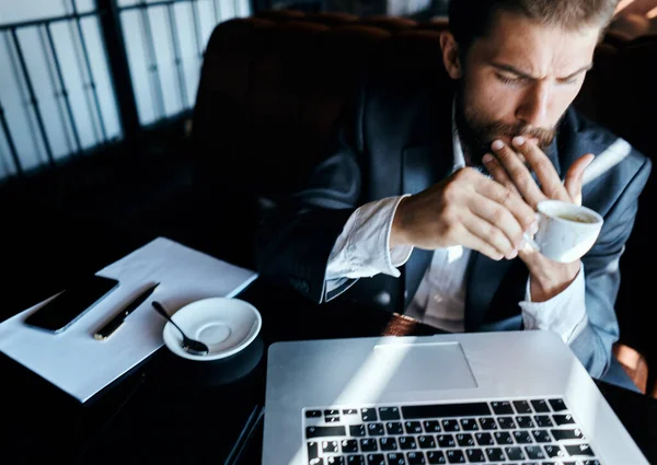 Uomo d'affari seduto in un caffè con una tazza di caffè tra le mani di fronte a una comunicazione tecnologia portatile — Foto Stock