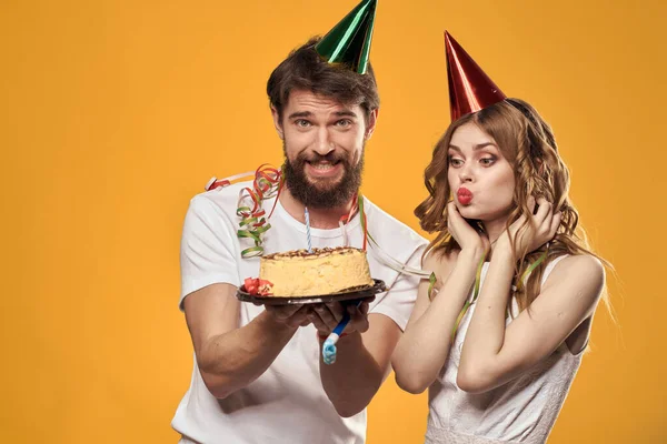 Man och kvinna födelsedag festlig tårta gul bakgrund och mössor på huvudet — Stockfoto