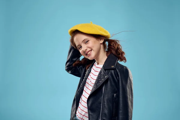 Krásná dívka s černou bundou a žlutý klobouk na hlavě červené vlasy model modré pozadí — Stock fotografie