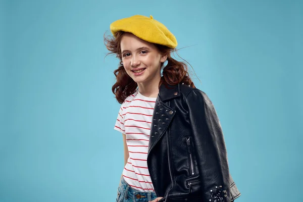 Mooi meisje met een zwart jasje en een gele hoed op haar hoofd rood haar model blauw achtergrond — Stockfoto