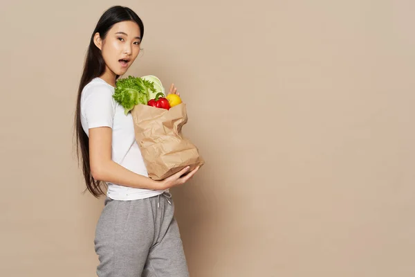 Mujer bonita en pantalones de chándal y una camiseta tiene un paquete de comestibles en sus manos —  Fotos de Stock