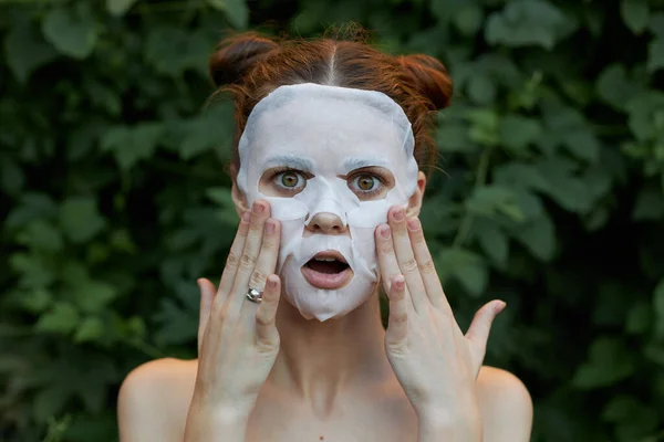 Schöne Frau Anti-Aging-Maske Überrascht, Ihr Gesicht mit Ihren Händen zu berühren nackten Schultern Büsche im Hintergrund — Stockfoto