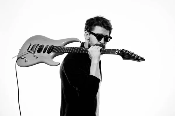 Mężczyzna trzyma gitarę w dłoniach czarna skórzana kurtka ciemne okulary muzyka wydajność lekkie tło — Zdjęcie stockowe