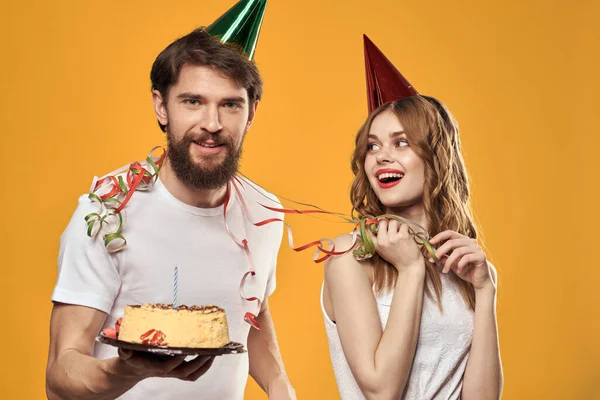 Muž a žena narozeniny slavnostní dort žluté pozadí a čepice na hlavě — Stock fotografie