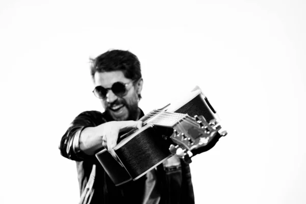 一个男人穿着黑色皮夹克，戴着浅色背景的太阳镜，弹吉他 — 图库照片