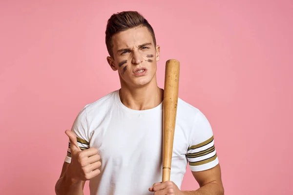 Energisk man med ett slagträ på en rosa bakgrund T-shirt ansikte make-up svarta linjer aggression modell — Stockfoto