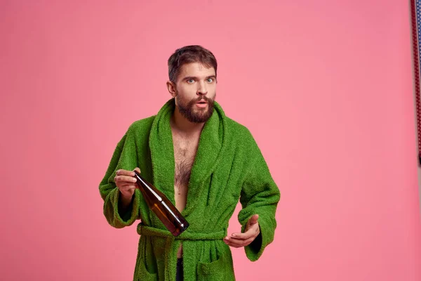 Homem bêbado com uma garrafa de álcool na mão em um fundo rosa vista cortada de um manto verde — Fotografia de Stock