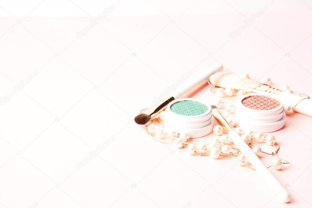 Makeup brushes, eyeshadows, decorative cosmetics and beads on a light background
