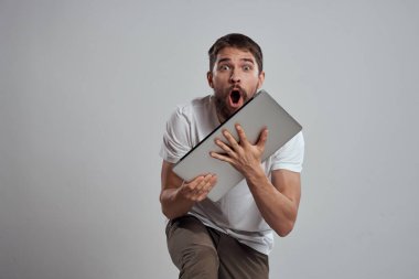 Elinde dizüstü bilgisayarla beyaz tişörtlü bir arka planı olan bir adamın duyguları yeni teknolojileri aydınlatır.