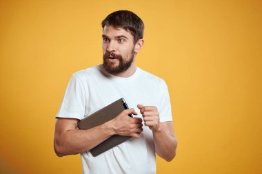 Beyaz tişörtlü, sarı arka planda tabletli bir adam. Yeni teknoloji işadamı ekranda dokunuyor.