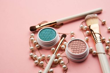 Göz falı aksesuarlar, boncuklar makyaj fırçaları pembe arka planda profesyonel kozmetik ürünleri koleksiyonu.