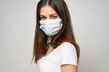 Yüzünde tıbbi maske olan bir kız. Önüne bak. Uzun saçlı, beyaz tişörtlü. 