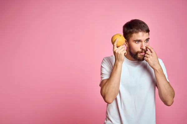 Jongeman met oranje op een roze achtergrond in een wit t-shirt emoties leuk gesticuleren met model handen — Stockfoto